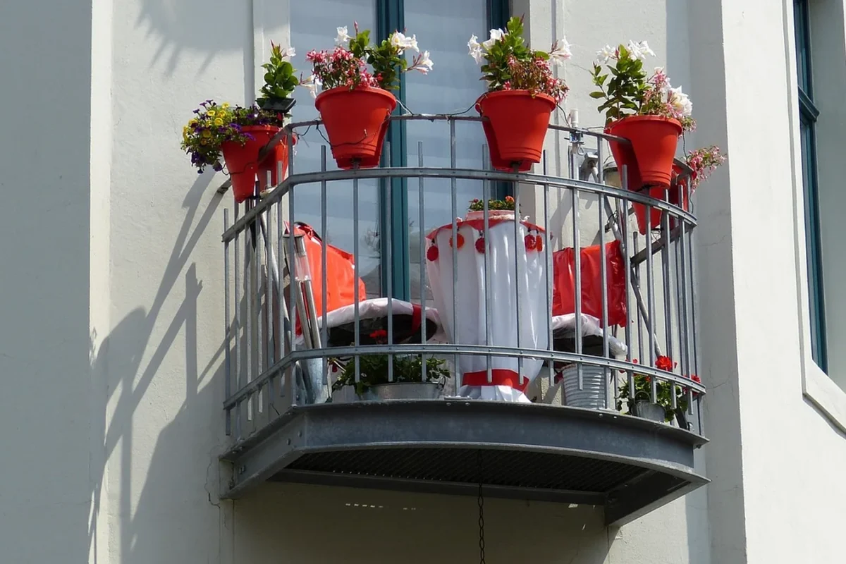 Balcon d'immeuble au garde-corps garni de pots rouges fleuris